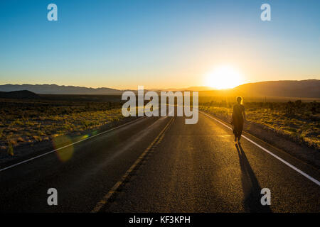 Donna che cammina verso il basso una lunga strada tortuosa al tramonto nella parte orientale del Nevada, Stati Uniti d'America Foto Stock