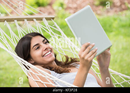 Sorridente ragazza rilassante in amaca con tavoletta digitale Foto Stock