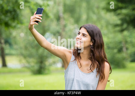 Giovane donna sorridente tenendo Selfie dal telefono cellulare Foto Stock