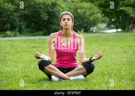 Giovane donna seduta su erba meditando in posizione di parcheggio Foto Stock