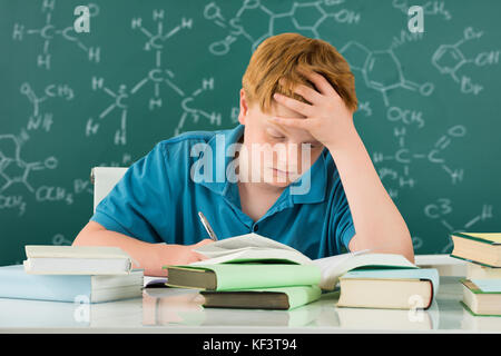 Stanco ragazzo studiare in aula con libri sulla scrivania Foto Stock