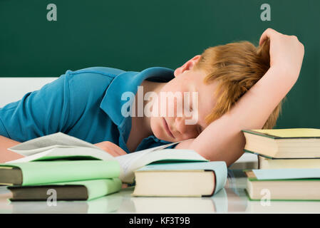 Bambino addormentato in aula con libri sulla scrivania Foto Stock