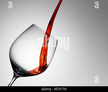 Vino rosso versato in elegante bicchiere di vino sul gradiente grigio Foto Stock