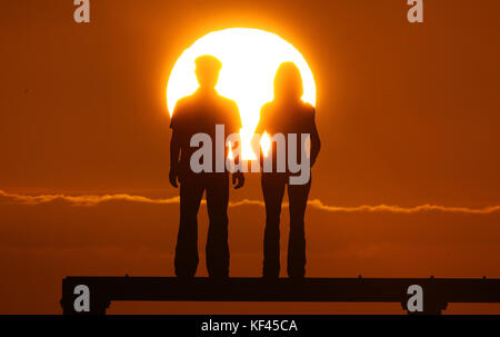 Il sole sorge sopra la scultura di coppia di Sean Henry sulla costa del Mare del Nord a Newbiggin Bay in Northumberland. Foto Stock