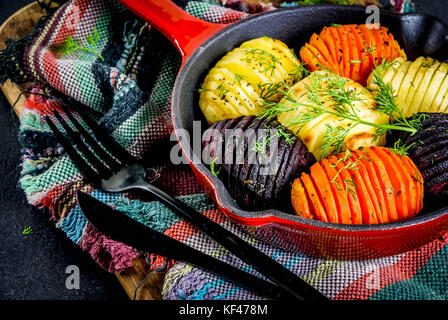 Idee di cibo vegan, autunno le ricette di verdure tostate hasselback barbabietole, carote, patate, con erbe fresche, in una padella, su una pietra nera Foto Stock
