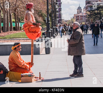 Indian gli artisti di strada in posa meditativa e indumenti di colore arancione con i turisti a guardare in Madrid Spagna, Europa. Foto Stock