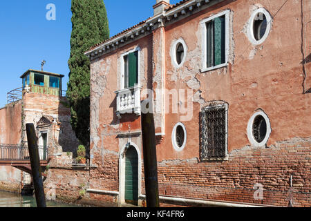 Dettagli architettonici di una antica casa, Giudecca, Venezia, Italia con grazioso weathered pareti in mattoni rossi, peeling intonaco e finestre a tutto sesto su un cana Foto Stock