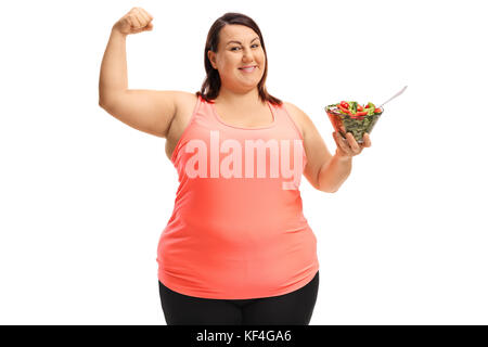 Donna sovrappeso flettendo il suo bicipite e tenendo una ciotola di insalata isolati su sfondo bianco Foto Stock