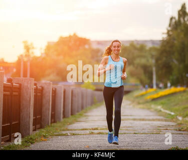 Giovane bella donna in corsa in posizione di parcheggio la mattina. ragazza sportiva jogging lungo argine Foto Stock