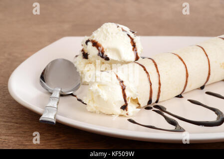 Primo piano di gelato alla vaniglia crêpe con salsa al cioccolato e cucchiaio Foto Stock