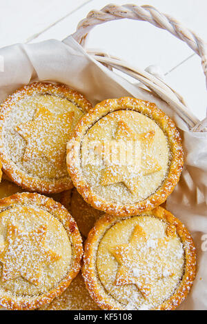 Tradizionale natale britannico pasticceria dolce cotto domestico pasticci di carne macinata con apple uvetta dadi il riempimento in cesto in vimini. golden pasta frolla in polvere bianca. Foto Stock