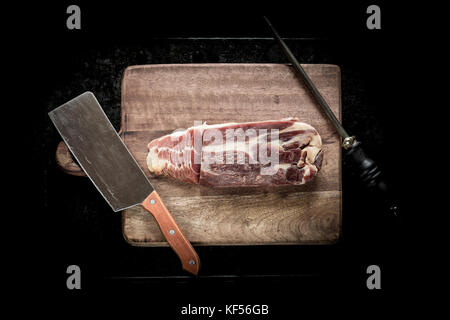 Fette di prosciutto su una tavola di legno, un coltello per carne e una mola Foto Stock