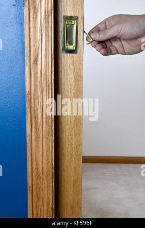 Close up view of a person unlocking a wooden pocket door with golden metal on side with their hand by lifting a lever Foto Stock