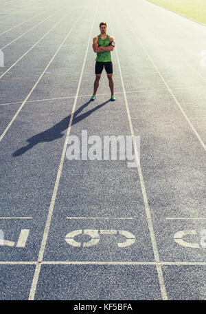 Runner permanente sulla via di corsa con le mani piegate. Atleta che indossa auricolari con telefono mobile fissato nella fascia braccio. Foto Stock
