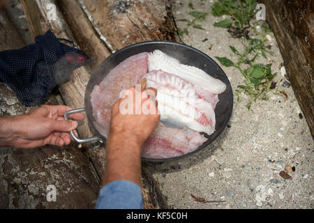 L'uomo il rovesciamento dei filetti di pesce mentre la frittura in padella Foto Stock