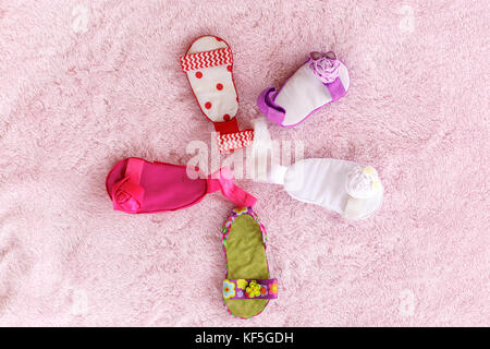 Cinque baby sandali di diverso colore disposti in una forma circolare contro un pallido sfondo rosa Foto Stock