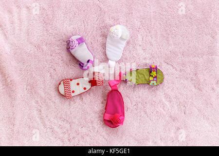 Cinque baby sandali di diverso colore disposti in una forma circolare contro un pallido sfondo rosa Foto Stock