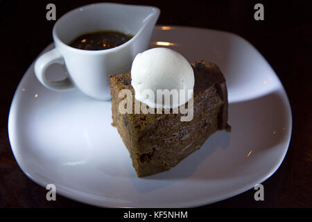 Sticky toffee pudding servito con gelato alla vaniglia. una brocca di salsa, cucita con noci pecan, sorge accanto al tradizionale dessert britannico. Foto Stock
