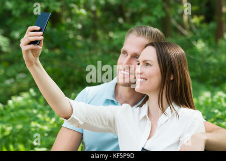 Giovane coppia felice di scattare una foto con lo smartphone in posizione di parcheggio Foto Stock