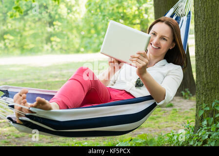 Giovane donna felice con tavoletta digitale durante i momenti di relax in amaca Foto Stock