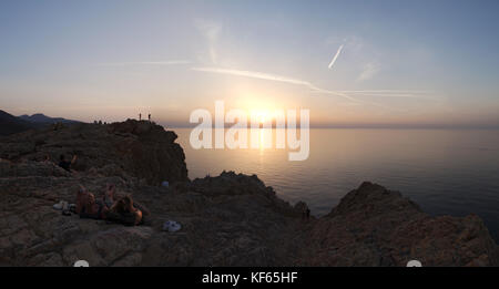 Corsica: la gente guardando il tramonto sul mar Mediterraneo dalla parte superiore dell'Ile de la pietra (stone island), il promontorio di Ile Rousse (isola rossa) Foto Stock