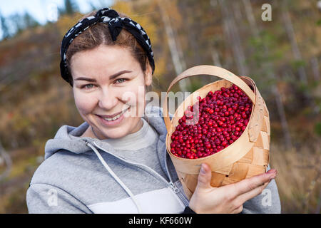 Giovane donna sorridente holding hands cesto pieno di ripe rosso mirtilli neri Foto Stock