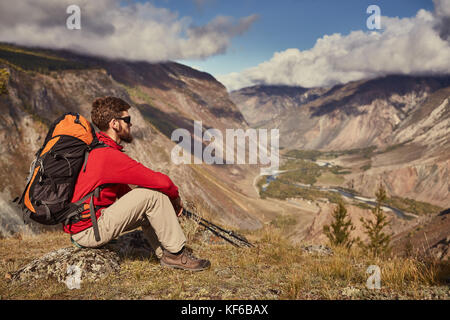 Bel giovane maschio escursionista seduta sul bordo di un canyon che guarda lontano Foto Stock