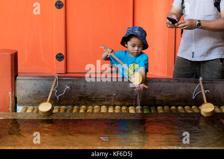 Miyajima - Giappone, 26 maggio 2017: il bambino è la pulizia delle mani a una fontana di purificazione del famoso tempio di Itsukushima sull miyajima Foto Stock