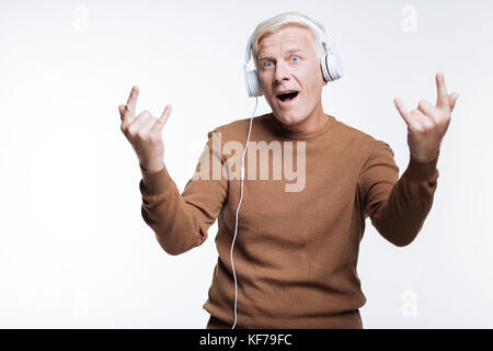 Senior uomo che ascolta musica e che mostra segni di corna Foto Stock