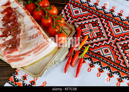 Un grande pezzo di pancetta cotta in forno con le spezie e le erbe su una carta con pomodori marinati. La vista dall'alto. Foto Stock