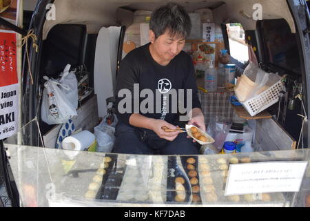 Uomo giapponese preparazione takoyaki, una tipica merenda a base di frumento a base di farina di pastella con pezzi di polpo all'interno Foto Stock