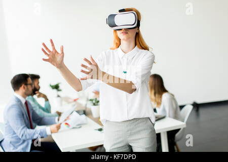 Imprenditrice eccitato in realtà virtuale bicchieri cercando di toccare cyber oggetti mentre altre persone di affari hanno sale riunioni Foto Stock