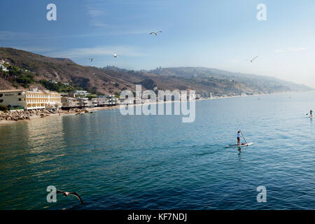 Stati Uniti, California, Malibu, crociera paddleboarders dal Malibu pier con il Malibu Beach inn a distanza Foto Stock