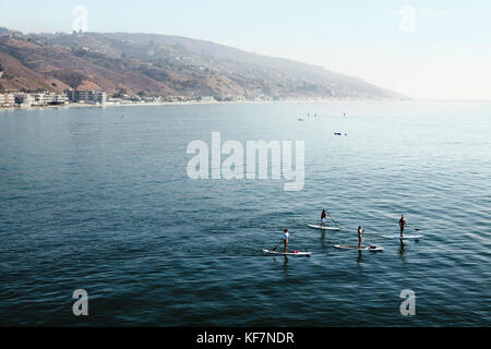 Stati Uniti, California, Malibu, quattro paddleboarders passano dal Malibu pier sul mare calmo, guardando verso sud lungo la costa di malibu Foto Stock