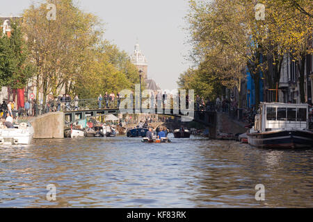 Vista dal livello dell'acqua di un canale in una città vivace, con gente che si riunisce su un ponte ad arco. Foto Stock
