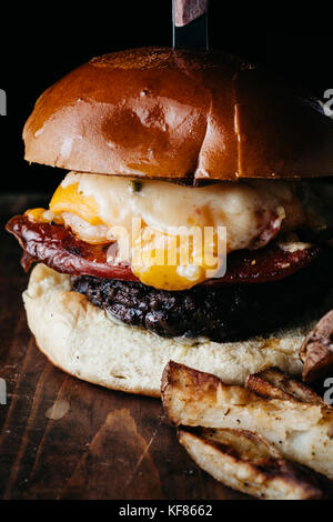 Giganic burger con chorizo e un uovo fritto servito con patate fritte su scuro dello sfondo rustico Foto Stock