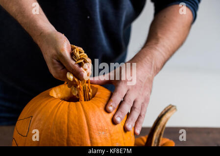 Mani maschio carving zucca tenendo fuori i semi Foto Stock