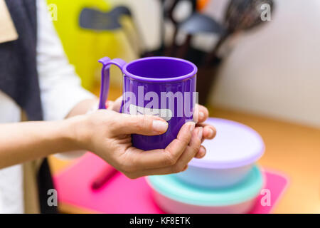 Tenere le mani una tazza di plastica con il volto sorridente Foto Stock