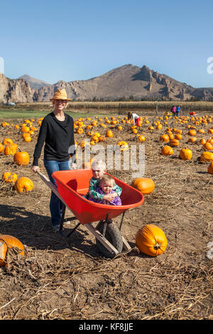 Stati Uniti d'America, oregon, piegare una madre ruote intorno ai suoi due bambini possono sedersi dentro una carriola all'annuale zucca patch situato in terrebone vicino a Smith ro Foto Stock