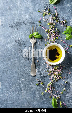 Giovani germogli di rafano con rosa sale himalayano e le foglie di basilico con coppa di olio di oliva e aceto balsamico e blu su sfondo texture. vista superiore con Foto Stock