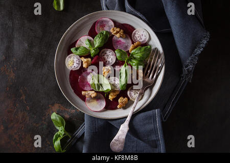 Vegano carpaccio di barbabietole da insalata di radicchio, basilico, olio d'oliva e le noci a piastra in ceramica oltre il buio metallo arrugginito sfondo. top view, spazio. dark ruggine Foto Stock