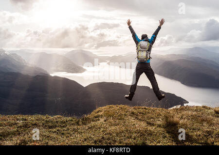 L'uomo raggiungendo il culmine e saltando di gioia. splendida vista alle montagne costiere e fiordi. hellandsnuten, sandsfjord, Norvegia. Foto Stock