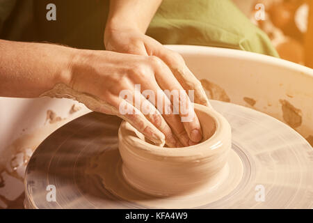 Close-up di una giovane donna potter splendidamente scolpisce un marrone vaso di creta e rende il suo collo su un tornio del vasaio, una vista superiore Foto Stock