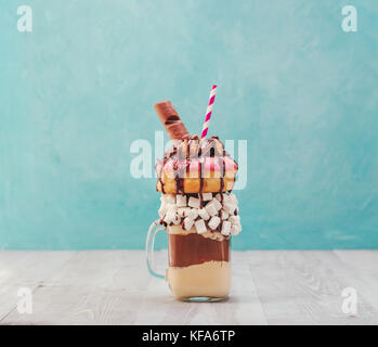 Il cioccolato e le ciambelle extreme frullato con marshmallow e altri dolci mason jar su grigio tavolo in legno e sfondo blu. Crazy freakshake su gr Foto Stock