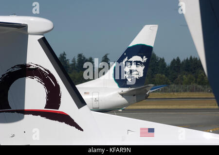 Tail-pinna di un orizzonte aria Bombardier DHC-8 Dash 8-400 Q400 parcheggiata con una coda fin di un Alaska Airlines Boeing 737 rullaggio dietro Foto Stock