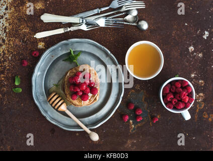 Set colazione. frittelle di farina di grano saraceno con lamponi freschi, miele e foglie di menta su grunge sfondo metallico, vista dall'alto, il fuoco selettivo Foto Stock