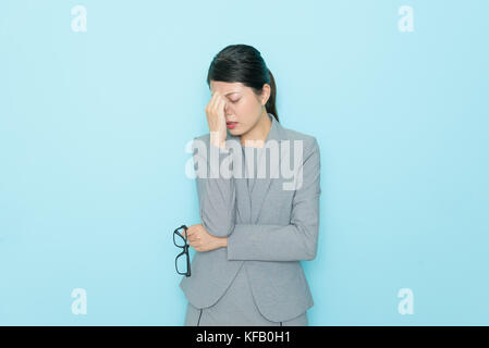 Giovane professionista lavoratore di ufficio lady lavorando a lungo tempo e sensazione di stanchezza che mostra permanente dolorosa in blu sullo sfondo della parete office. Foto Stock