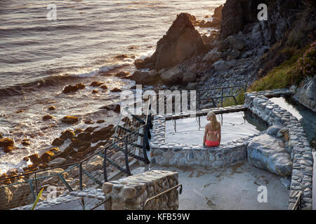 Stati Uniti, California, Big Sur, esalen, una donna si siede sul bordo della primavera calda ai bagni e prende la sera vista il Esalen Institute Foto Stock