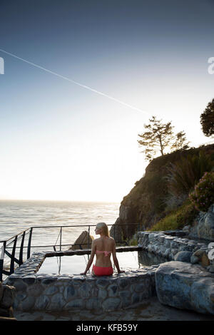 Stati Uniti, California, Big Sur, esalen, una donna si siede sul bordo della primavera calda ai bagni e prende la sera vista il Esalen Institute Foto Stock