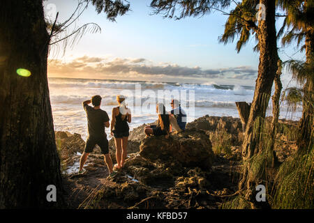 Hawaii, Oahu, North Shore, astanti guardare un grande rigonfiamento in rotolo al tramonto a pupukea beach park sulla sponda nord Foto Stock